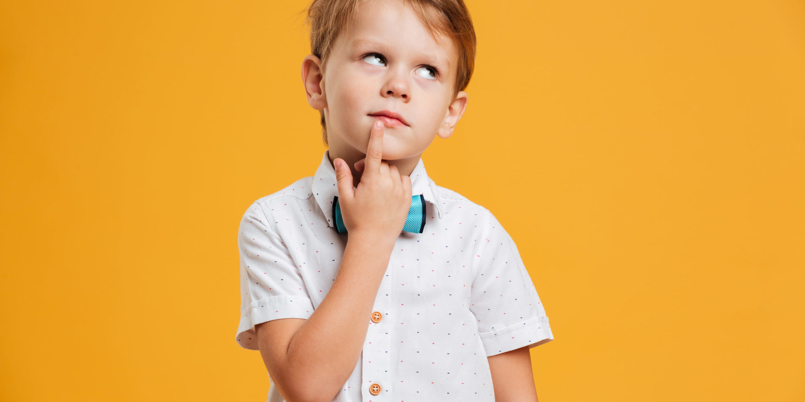 A little boy thinking with one finger on lips and looking upwards